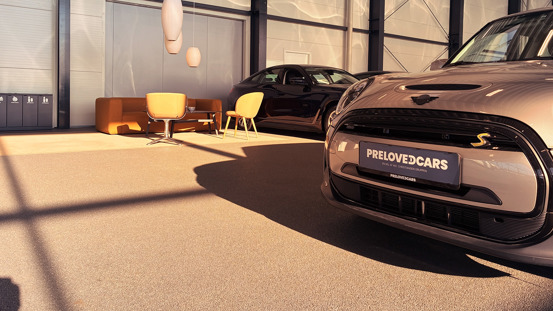PreLovedCars udstillingslokale med med en MINI, en brun sofa, to gule stole og en anden bil i baggrunden.